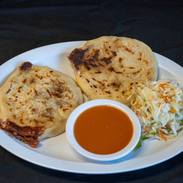 Two Salvadoran pupusas with curtido and a small bowl of red sauce on a white plate.