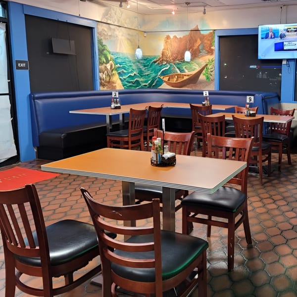 Empty dining area with blue booths, orange tables, wooden chairs, and a large mural of a beach scene.