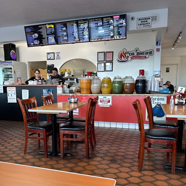 Interior of Los Cebollines Grill with tables, chairs, a counter with drinks, and staff behind it.