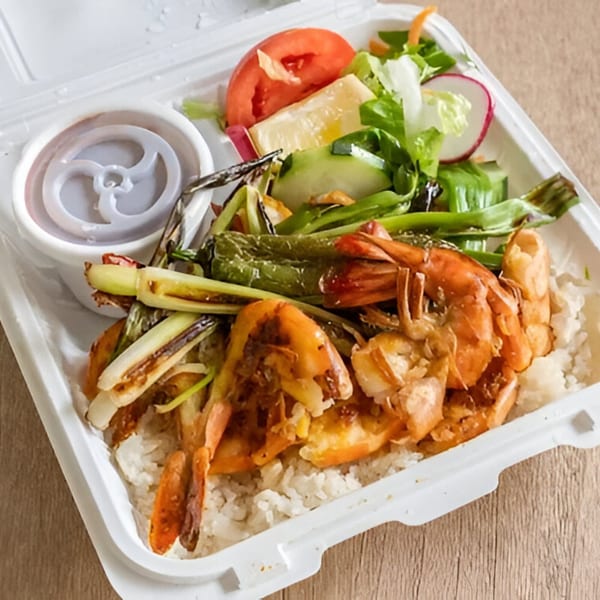 Grilled shrimp and vegetables over rice with a side salad and sauce in a white takeout container.