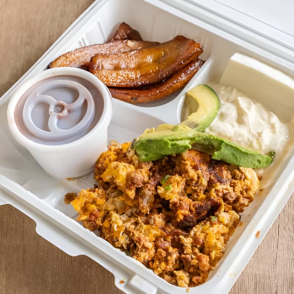 Salvadoran breakfast in a to-go container with scrambled eggs, plantains, avocado, sour cream, and cheese.