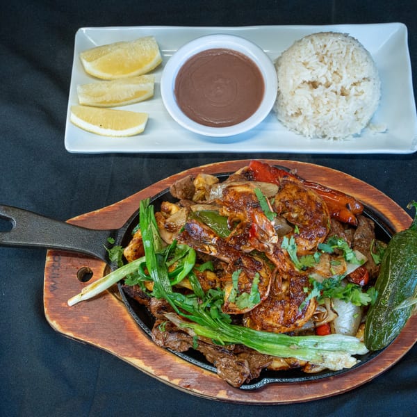 Sizzling fajitas with shrimp, beef, peppers, and onions, served with rice, beans, and lemon.