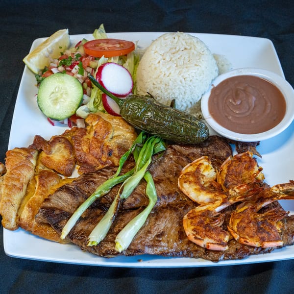 A large platter with grilled steak, shrimp, chicken, rice, beans, salad, and a jalapeño.