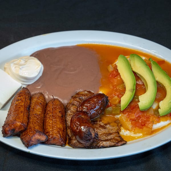 Salvadoran breakfast with plantains, sausage, steak, beans, eggs, avocado, and cheese.