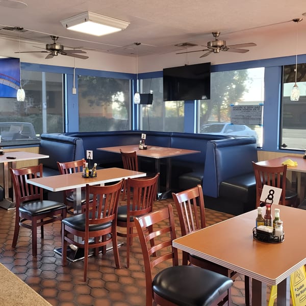 Empty dining area with blue booths, wooden chairs, and tables set with condiments at Los Cebollines Grill.